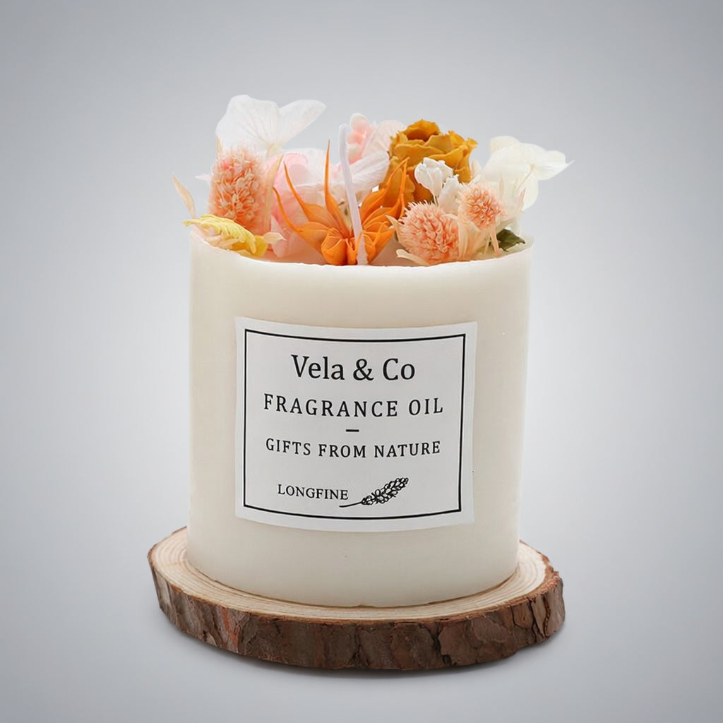 Vela Sanctuary scented candle topped with orange and peach dried flowers on a wood slice