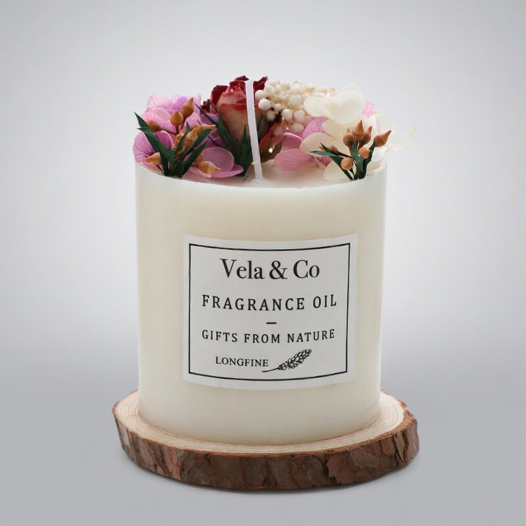 Vela Sanctuary scented candle topped with rose and burgundy dried flowers on a wood slice