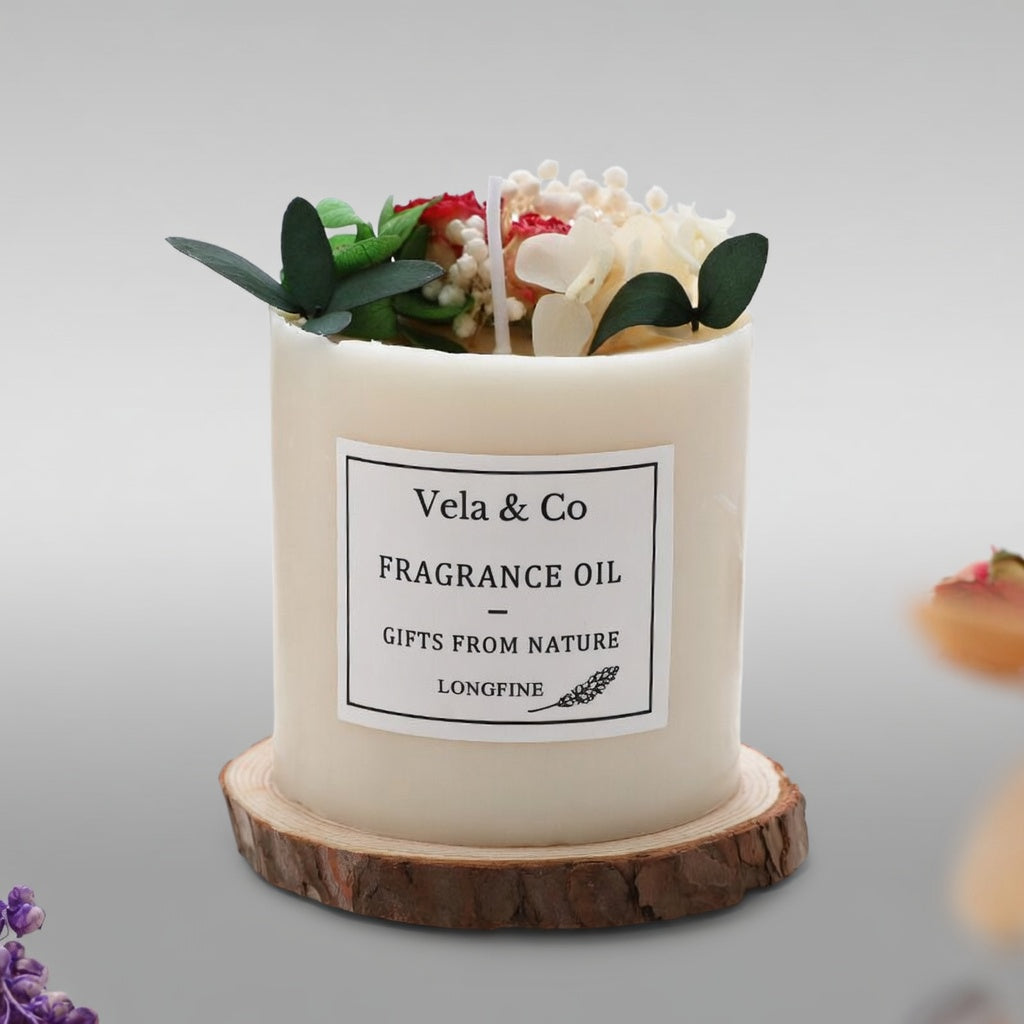 Vela Sanctuary scented candle topped with white roses and greenery on a wood slice