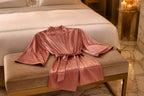 Vela Signature short satin kimono robe in rose laid on a bed bench